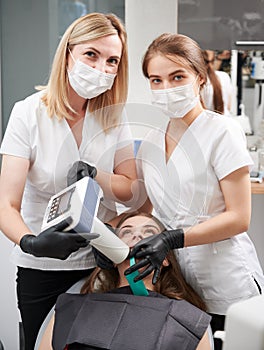 Dentist and assistant examining patient teeth with dental x-ray machine.