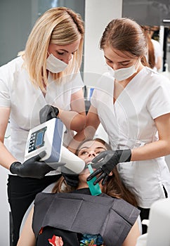 Dentist and assistant examining patient teeth with dental x-ray machine.