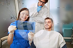 Dentist with assistant looking patientâ€™s X-ray of teeth