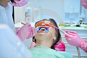 Dentist with assistant prepares woman patient for teeth whitening procedure