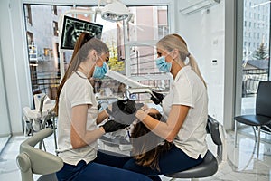 dentist and an assistant are professionally cleaning the teeth of patient in dental office.