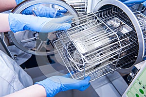 Dentist assistant`s hands get out sterilizing medical instruments from autoclave. Selective focus photo