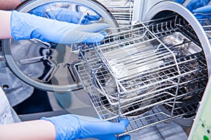 Dentist assistant`s hands get out sterilizing medical instruments from autoclave. Selective focus
