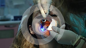 Dentist assistant shines with a polymerization UV lamp on the patient`s teeth. Visit to the stomatologist