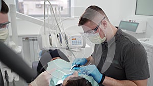 Dentist and assistant working in modern dental office. Doctor removes stones and hard plaque from teeth, assistant