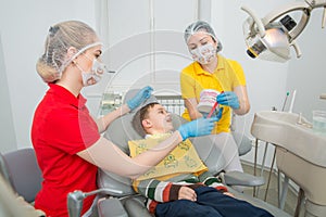 The dentist with assistent showing the little boy how to clean the teeth with a toothbrush on an artificial jaw dummy.