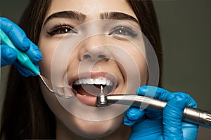 Dentist in blue gloves filling the beautiful smiling woman patient`s root canal under the medical lamp in clinic close up,