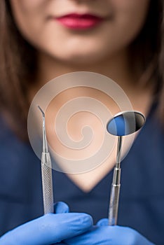 Dentist with blue gloves holding tools - dental mirror and dental probe at the dental office