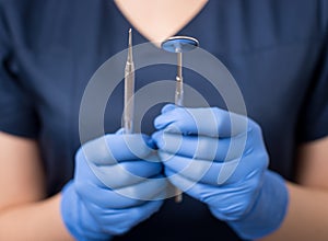 Dentist with blue gloves holding tools - dental mirror and dental probe at the dental office