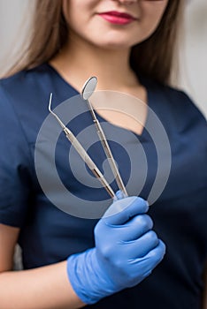 Dentist with blue gloves holding tools - dental mirror and dental probe at the dental office