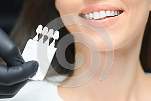 Dentist checking and selecting color of young woman's teeth