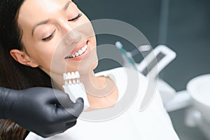 Dentist checking and selecting color of young woman's teeth
