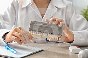 Dentist with color samples of teeth sitting at table in office