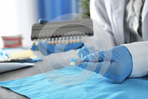 Dentist with color samples of teeth sitting at table in office, closeup