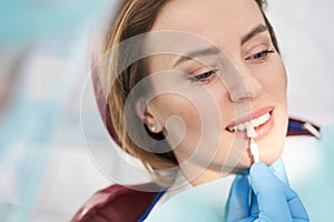 Dentist comparing color of woman teeth with dental implant