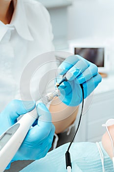 The dentist connects a sensor to the needle to remove the nerve in the tooth, holding it in his hands in blue gloves