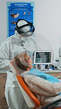 Dentist in coverall examining x-ray image on tablet