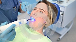 Dentist doctor using dental curing light equipment for filling, examining a patient`s teeth in dentistry office