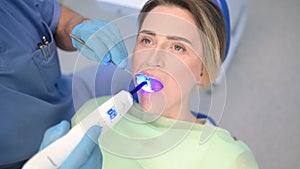 Dentist doctor using dental curing light equipment for filling, examining a patient`s teeth in dentistry office