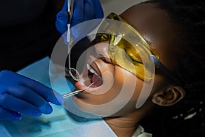 Dentist doing dental procedure in her office for woman patient in protective glasses