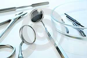 Dentist equipment: dental mirrors, spatula, kornzange or forceps, dental burs in Petri dish. Dental tools on blue glossy