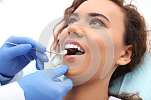 Dentist examining African-American woman`s teeth with mirror