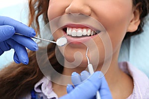 Dentist examining African-American woman`s teeth with probe and mirror