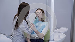 Dentist examining her patient teeth using dental tools and mirror at chair