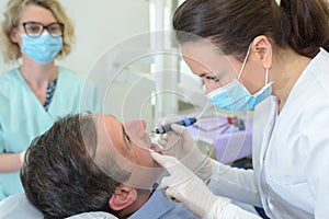 Dentist examining male patient with tools in clinic