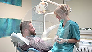 Dentist examining patient`s teeth explains him procedure. Slider shot, left.