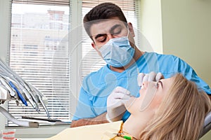 Dentist examining patient`s teeth, wearing blue uniform and gloves, looking at patient`s teeth carefully with dental instruments