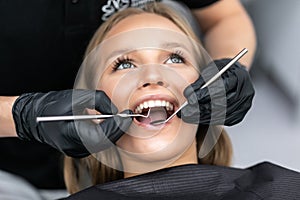 Dentist examining patient teeth with a mouth mirror and dental excavator. Close-up view on the woman`s face