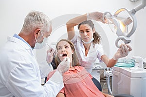 Dentist examining a patients teeth in the dentists chair with assistant