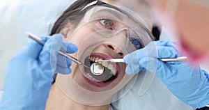 Dentist examining teeth of female patient wearing protective glasses using metal tools 4k movie slow motion