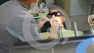 Dentist examining teeth with medical instruments. Portrait of young woman in glasses checking her teeth. Patient with