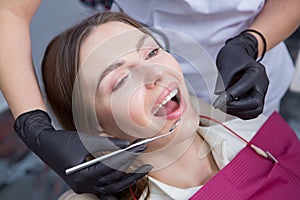 Dentist examining teeth of a young woman patient in a dental clinic.