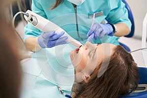 Dentist examining woman teeth with dental scanning device