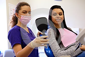 Dentist female showing her patient`s new teeth through the mirror in the dental cabinet.