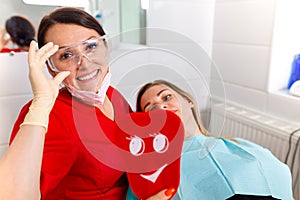 Dentist female showing her patient`s new teeth through the mirror in the dental cabinet. Patient is satisfied