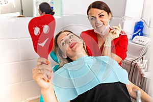 Dentist female showing her patient`s new teeth through the mirror in the dental cabinet. Patient is satisfied