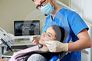 A dentist hands working on young woman patient with dental tools.