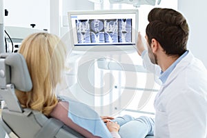 Dentist having conversation with female patient, poitning at LED display