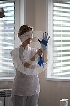 A dentist in her medical office wears blue uniform gloves on her hands.