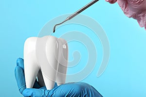 Dentist holding ceramic model of tooth and professional tool on color background photo