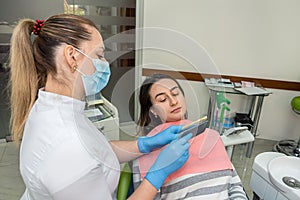 Dentist holding tooth samples for bleaching treatment choosing a shade for her young woman patient