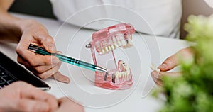 dentist implantologist showing dental implant technology on tooth jaw model to patient