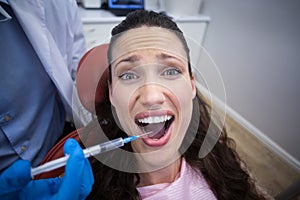 Dentist injecting anesthetics in scared female patient mouth photo