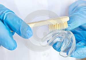 Dentist inserting retainers. Mouthguard with wooden toothbrush in doctors hands in blue gloves, teen orthodontic, Clear Aligner