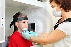 Dentist in mask prepares boy to jaw x-ray image