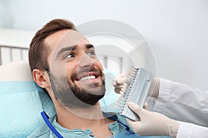 Dentist matching young man`s teeth color with palette